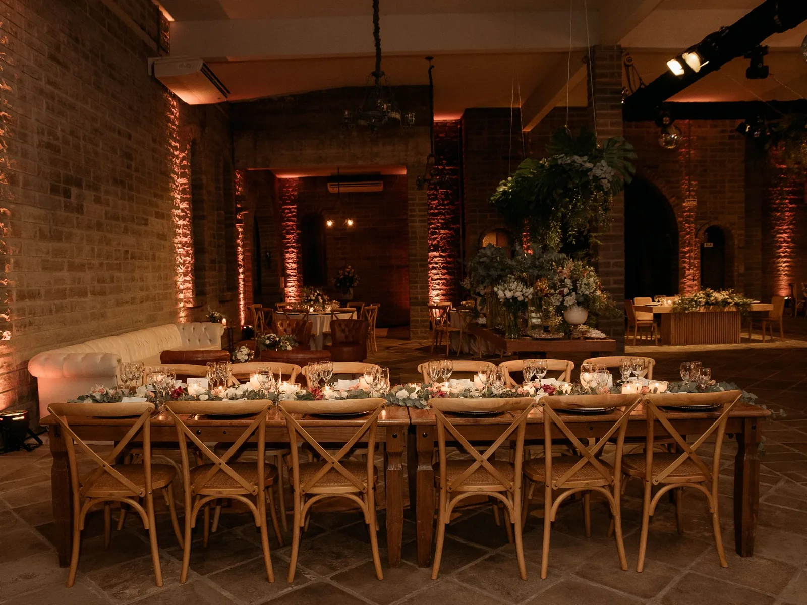 Candlelit long-table dinner with warm brick walls and sculptural greenery